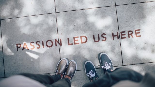 Decorative image: Picture focuses on the two peoples' feet, standing in front of some text on the floor, which says "passion led us here" 