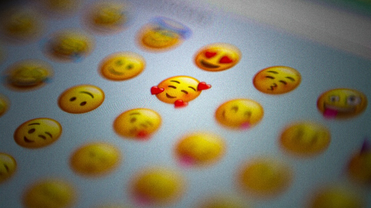 Decorative image, showing a close up of some emojis on a phone screen, centred on a face surrounded by hearts