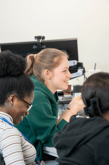 Three NTU students smiling and laughing as they engage in a classroom activity 
